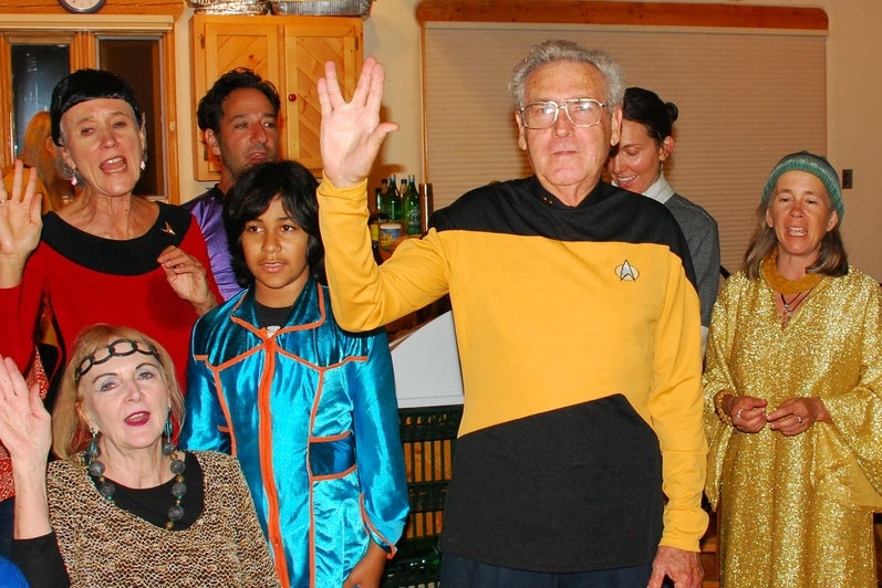 People in star trek uniforms hold hands up with middle and ring fingers spread.