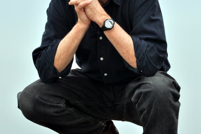 Man dressed in black with black cowboy hat crouches.