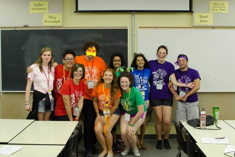 Group of university students wearing orientation gear standing at the front of a classroom and smiling
