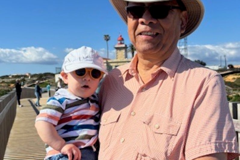 Man with white hat holds a babby in a striped shirt. 