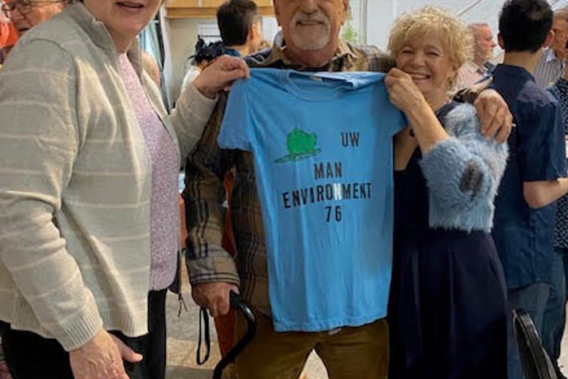 Three classmates from Man-Env '76 holding up a vintage tshirt