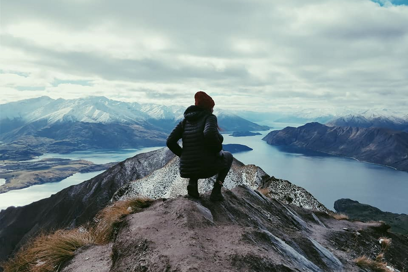 Female student standing on Roys Peak in New Zealand with her back to the camera, looking at the water.