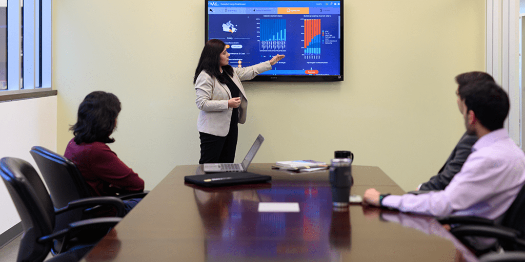 Person pointing to presentation slide in a meeting with three people.