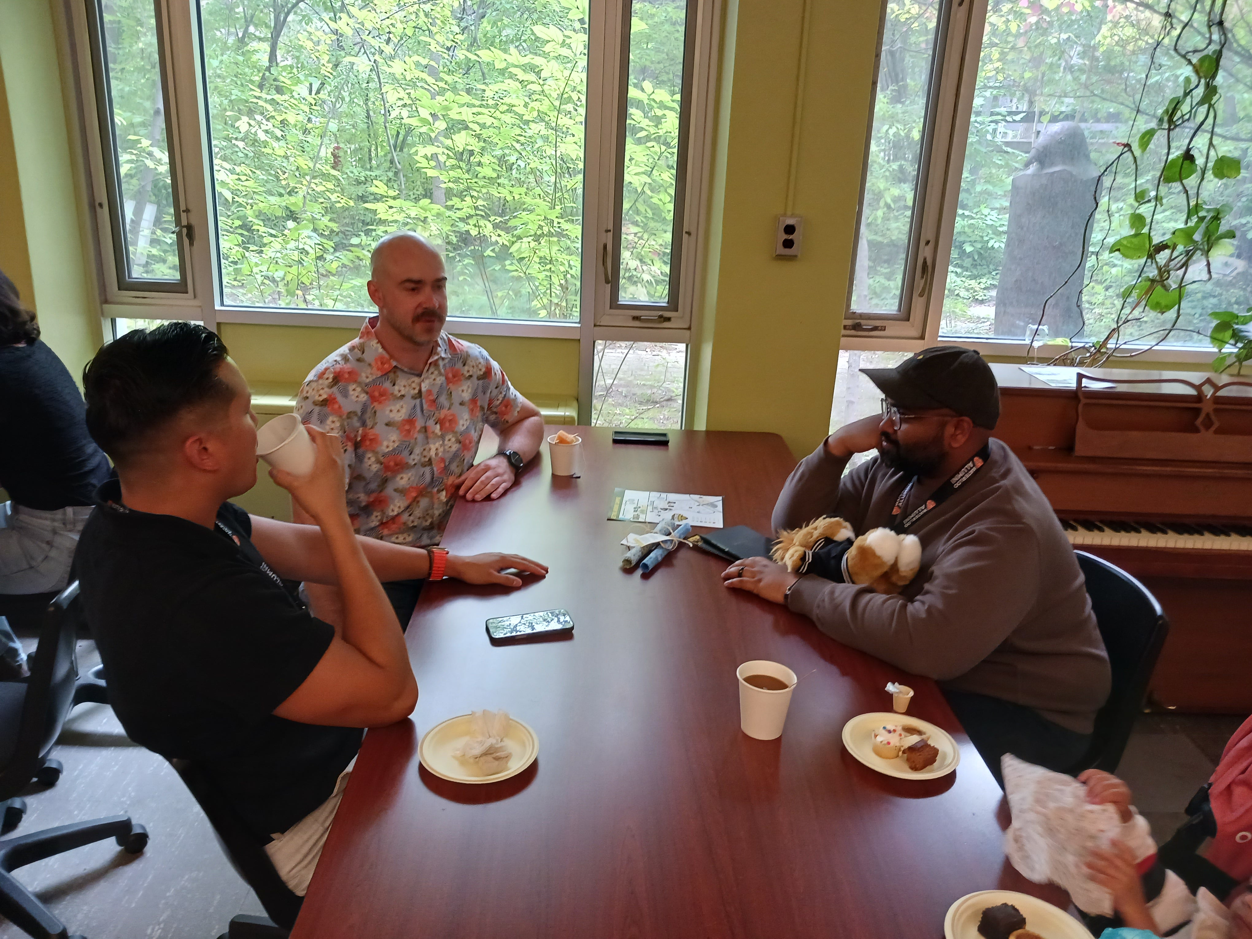 A group of three people sit at a table with coffees, talking. 