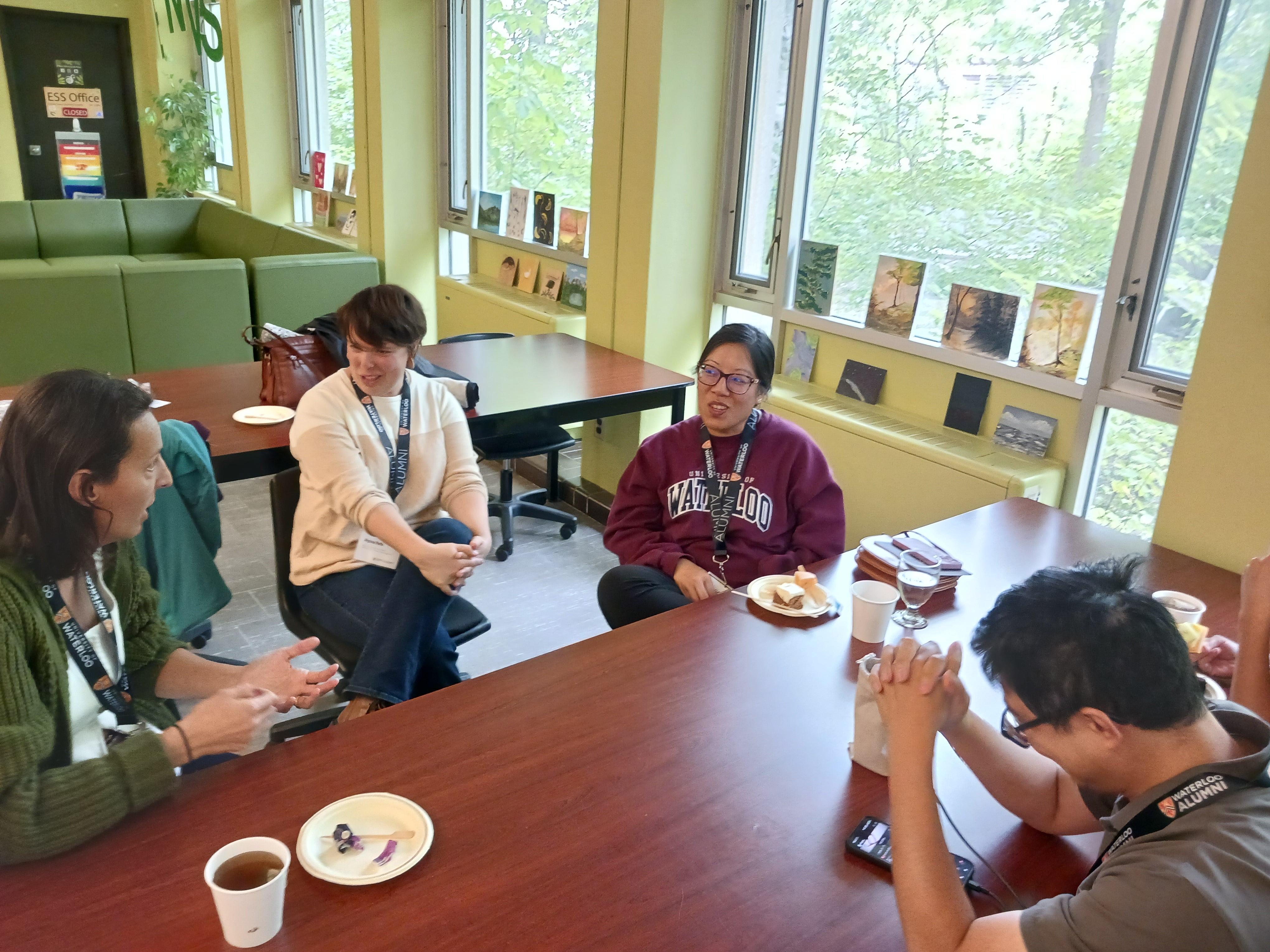 A group of four people sit at a table with coffees, talking. 