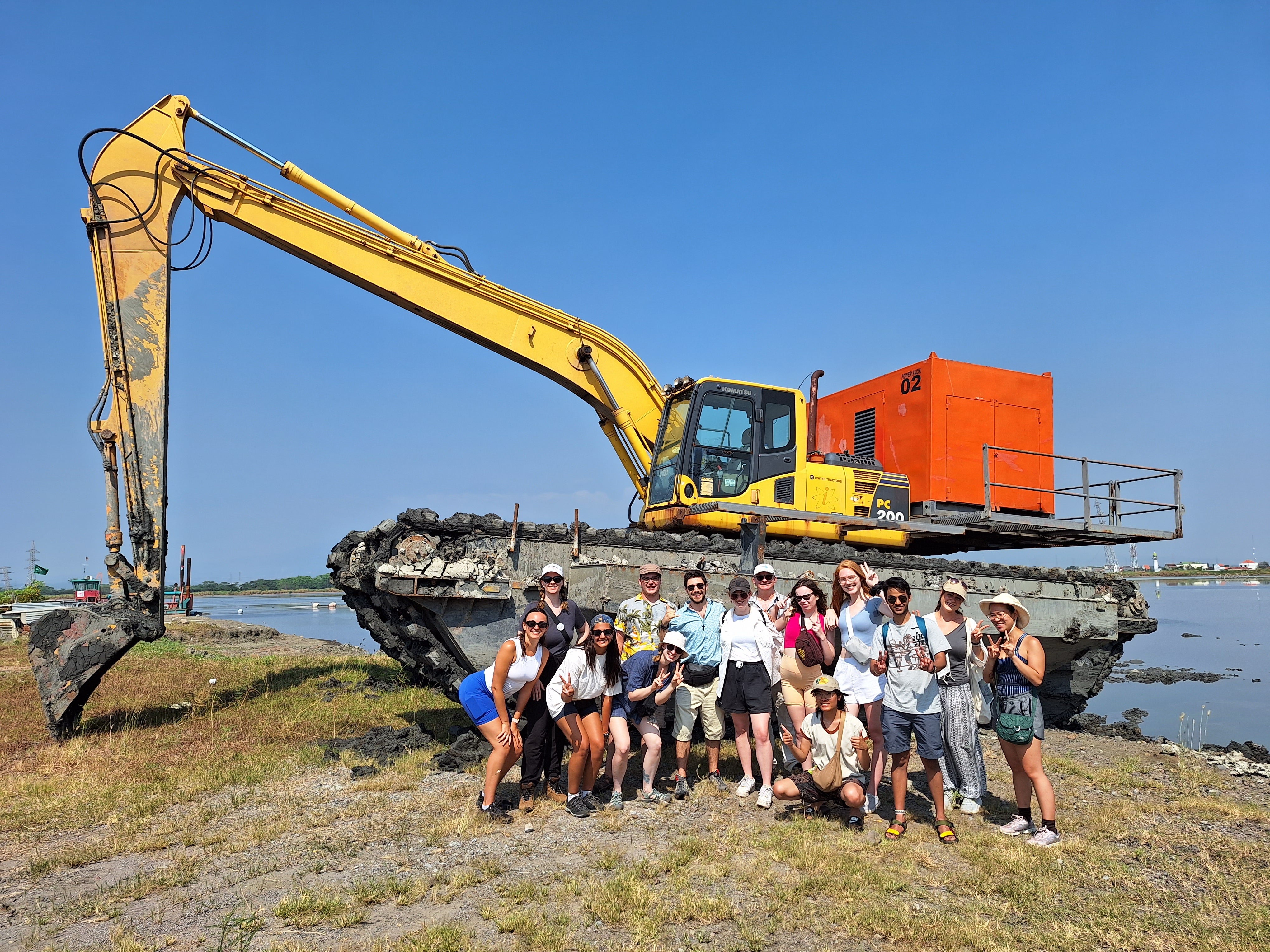 Group of students and professor in front of heavy machinery.