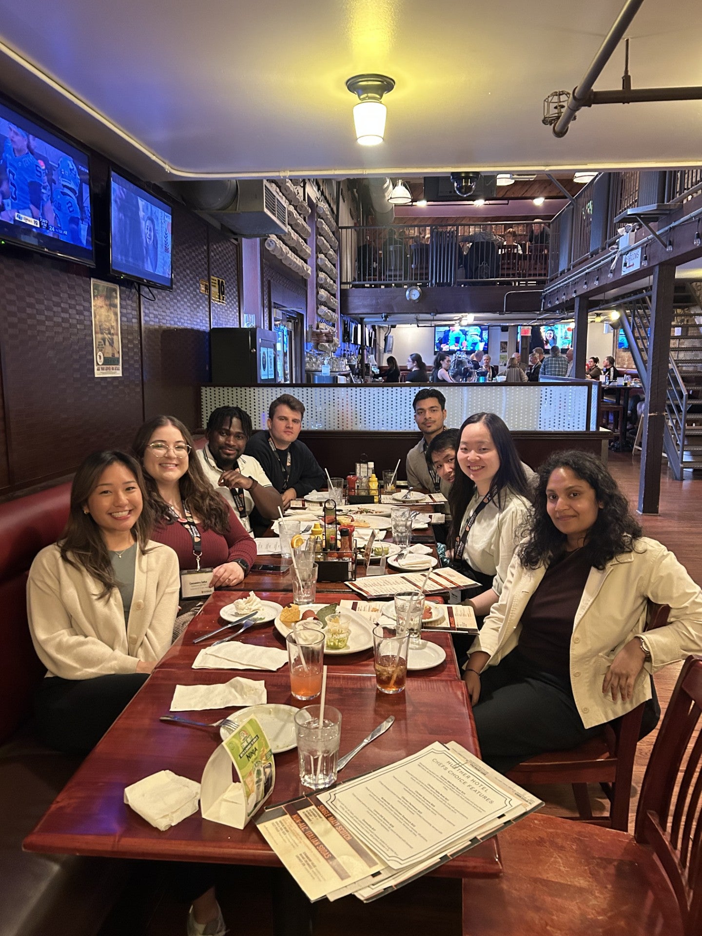 A group of people sitting around a table in a restaurant, with food and drinks on the table.