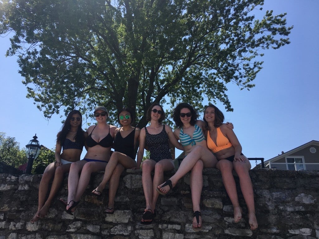 Six female university students in swimwear sitting on a wall and smiling