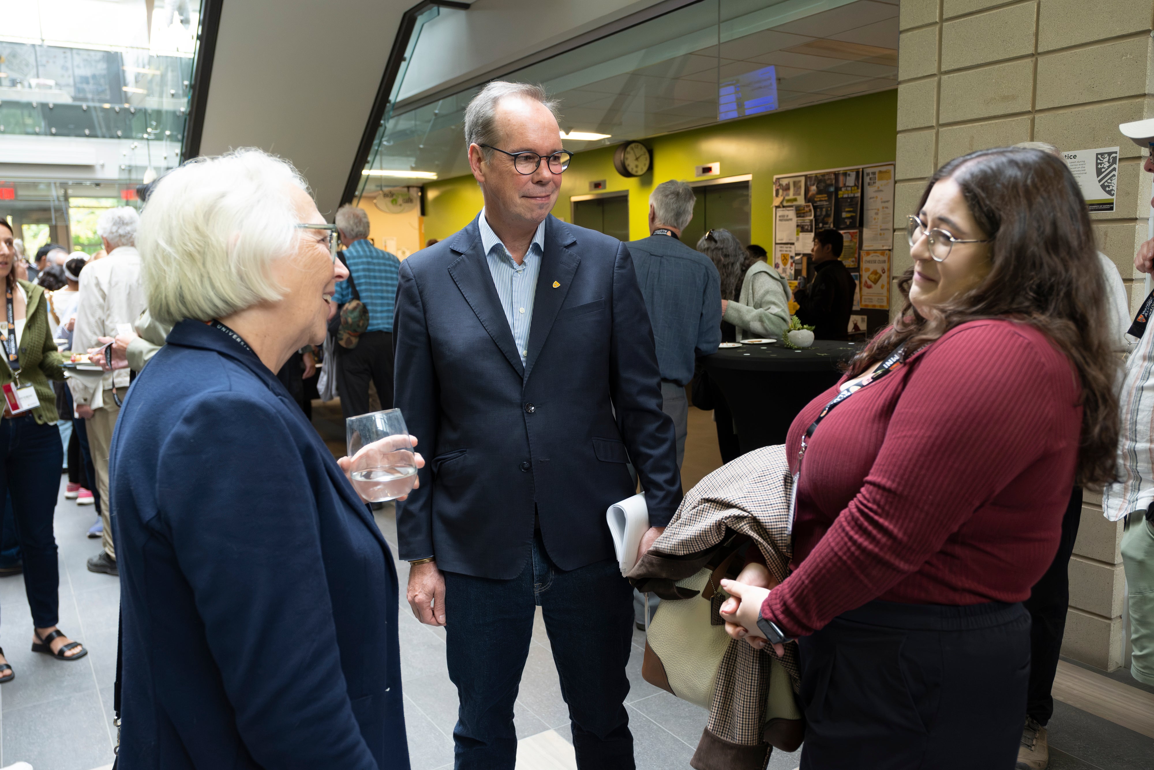 A group of people engaged in conversation, with one individual holding a drink and smiling.