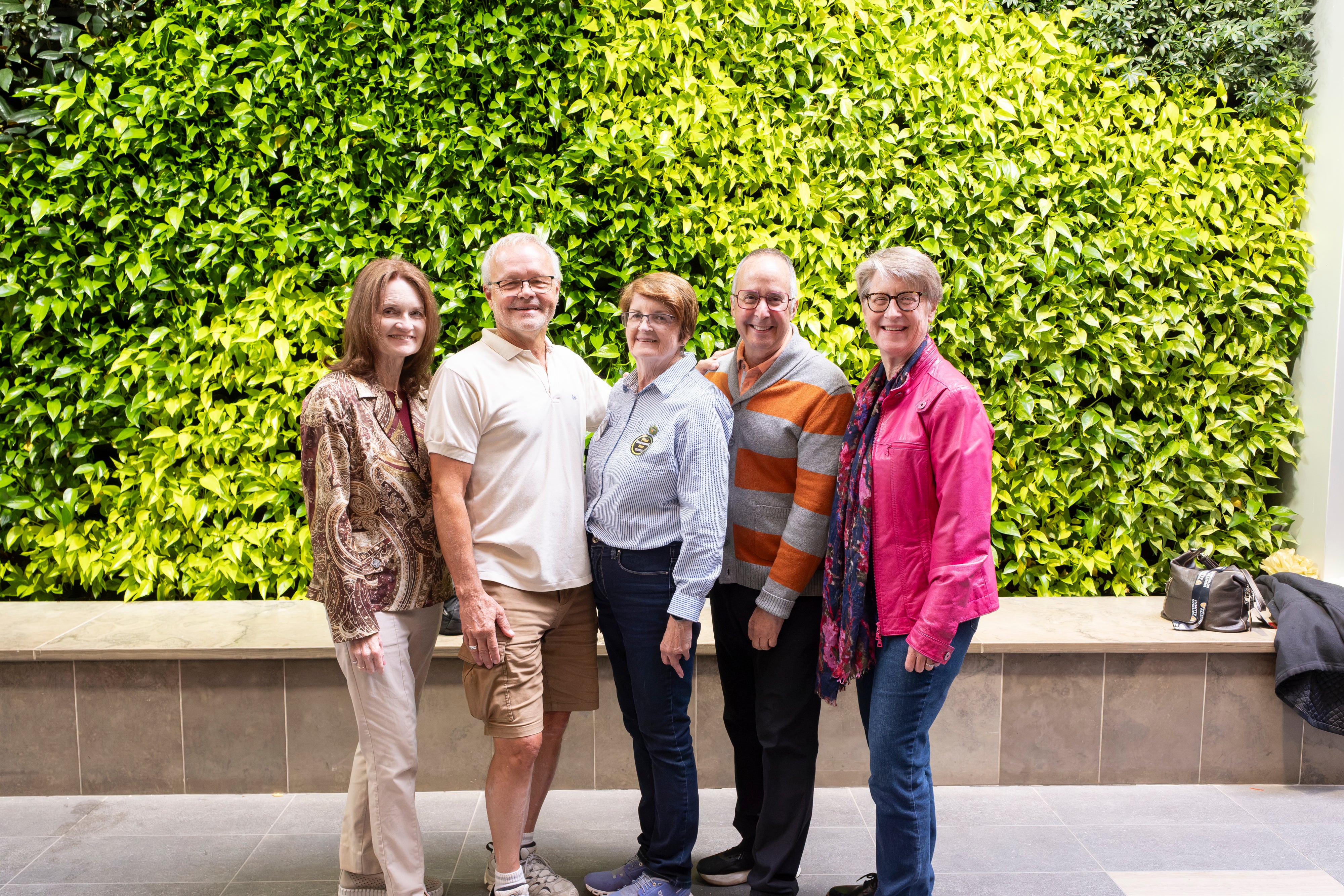 Five people stand in front of a green plant wall. 