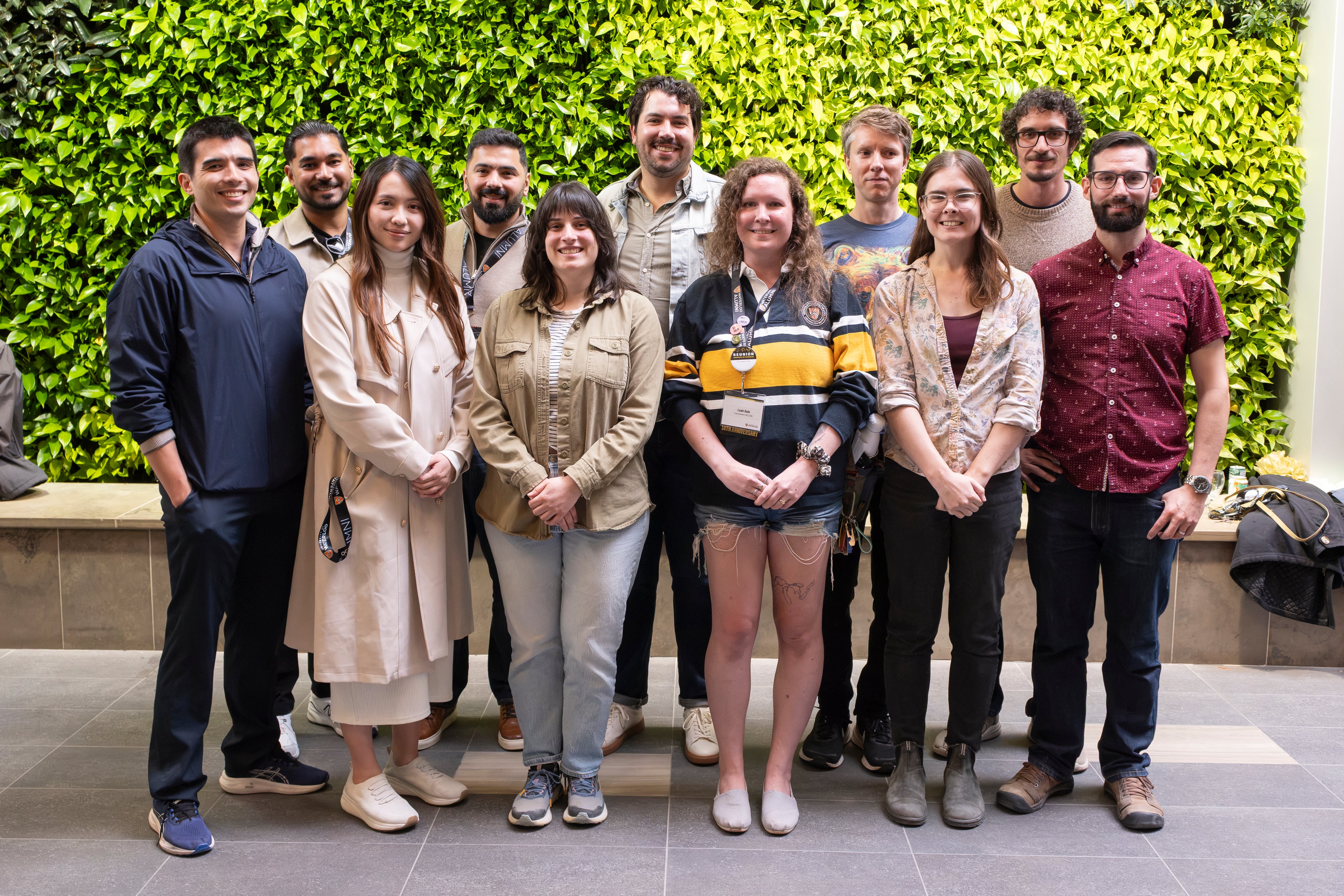 A group of eleven people posing together in front of a green wall.