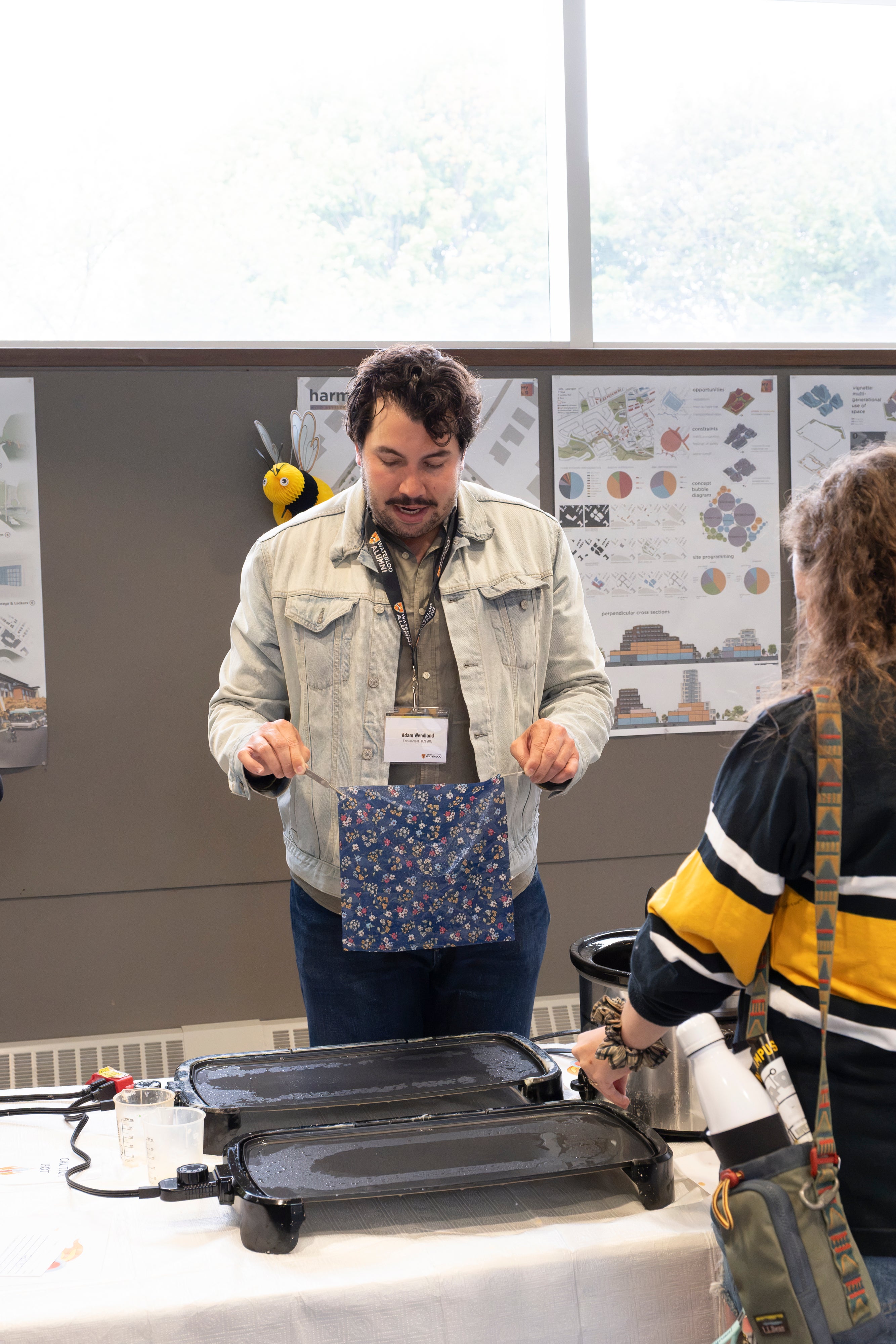 Two people stand at long table, making crafts.
