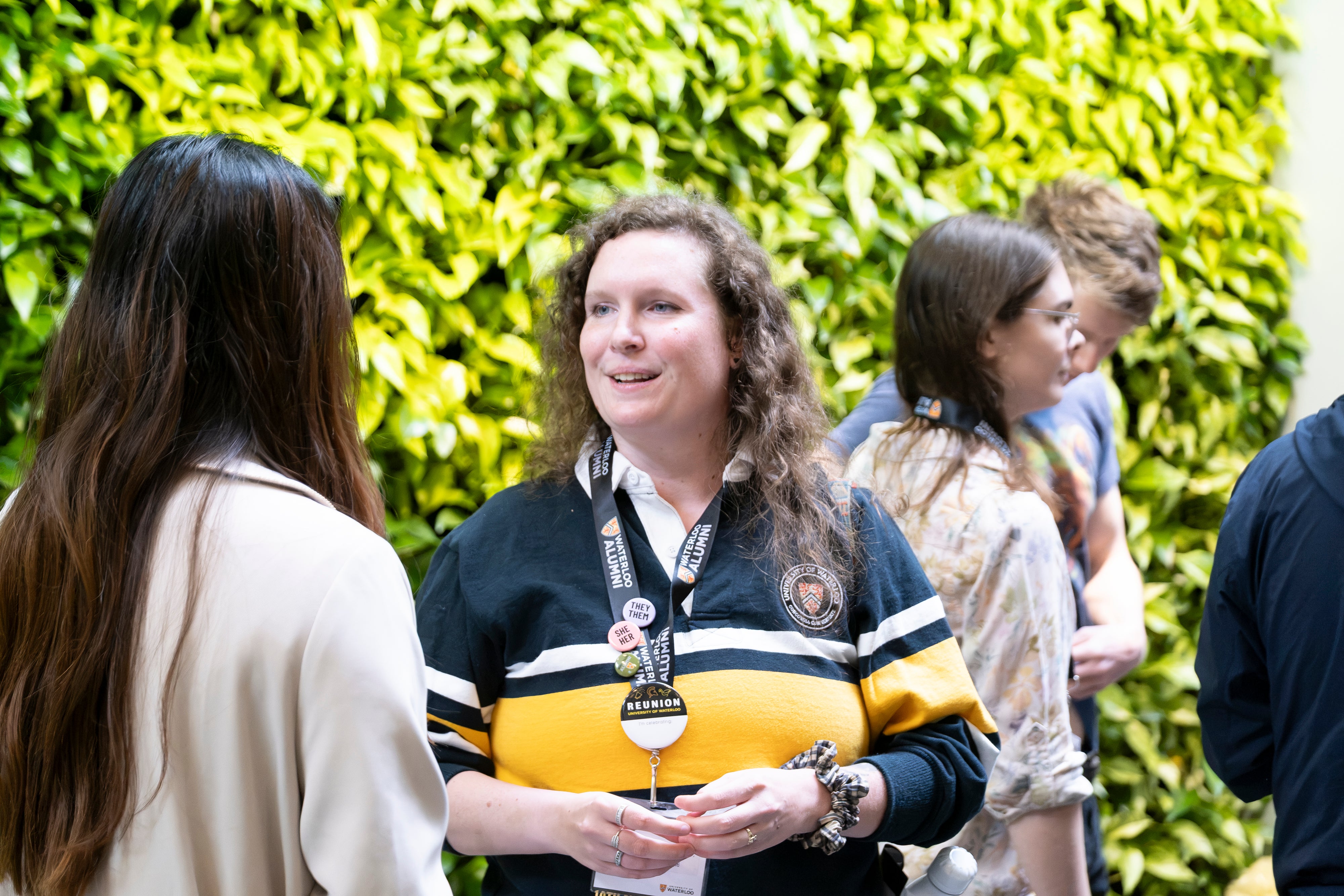 Two people engaging in conversation at a reception with a green plant wall in the background.