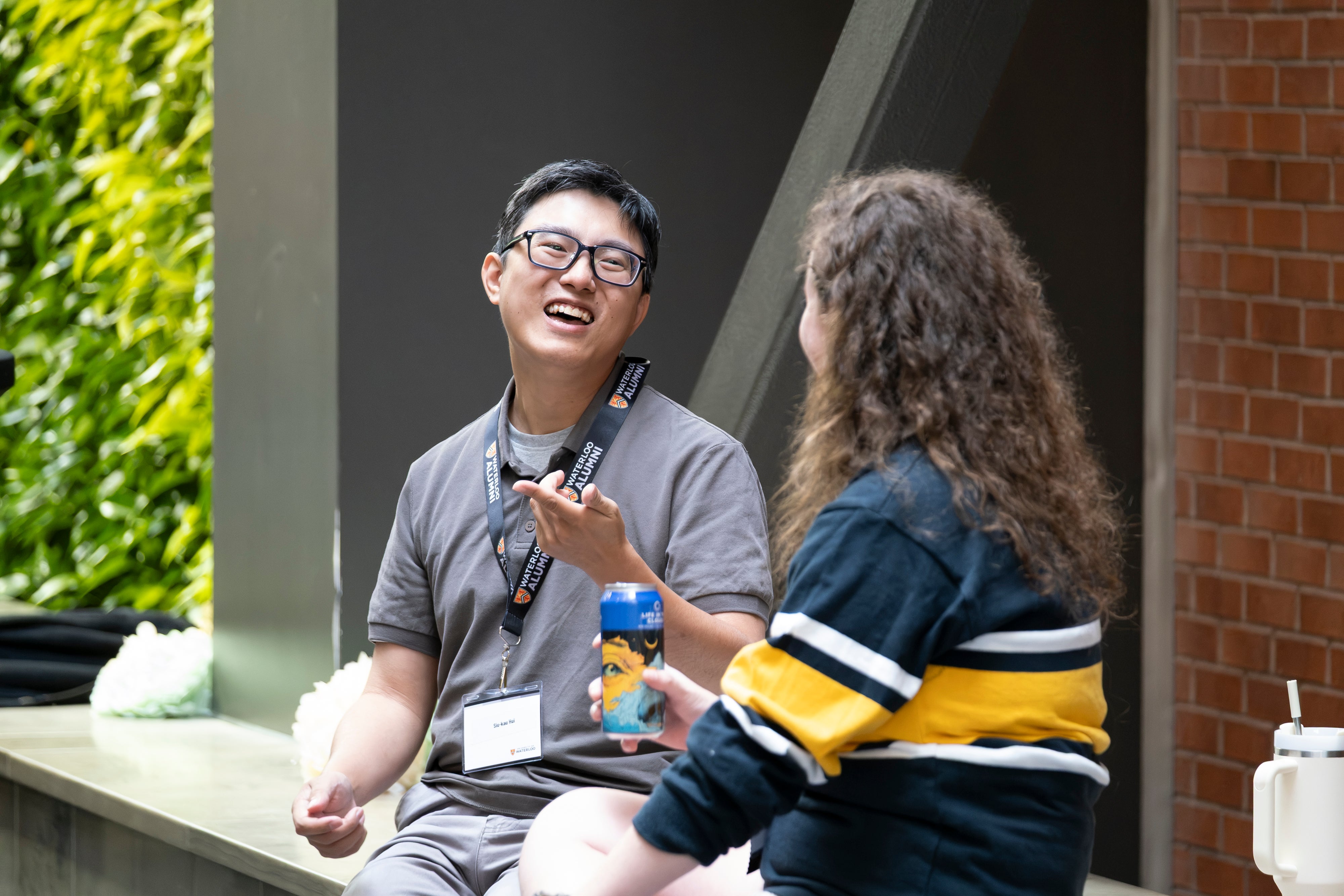 Two people engaging in conversation at a reception with a green plant wall in the background.