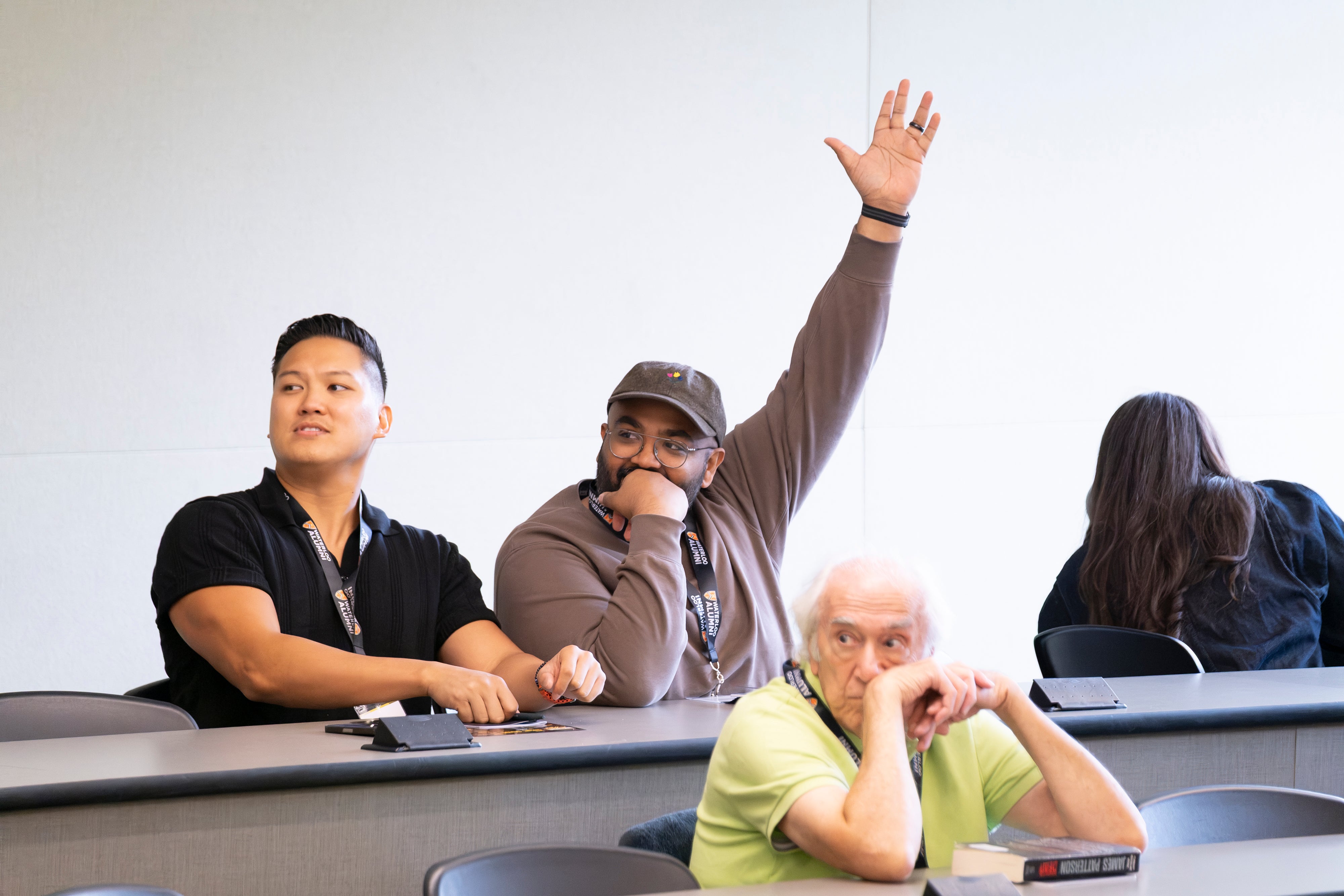 Two people sit in lecture hall, with one holding their hand up. 