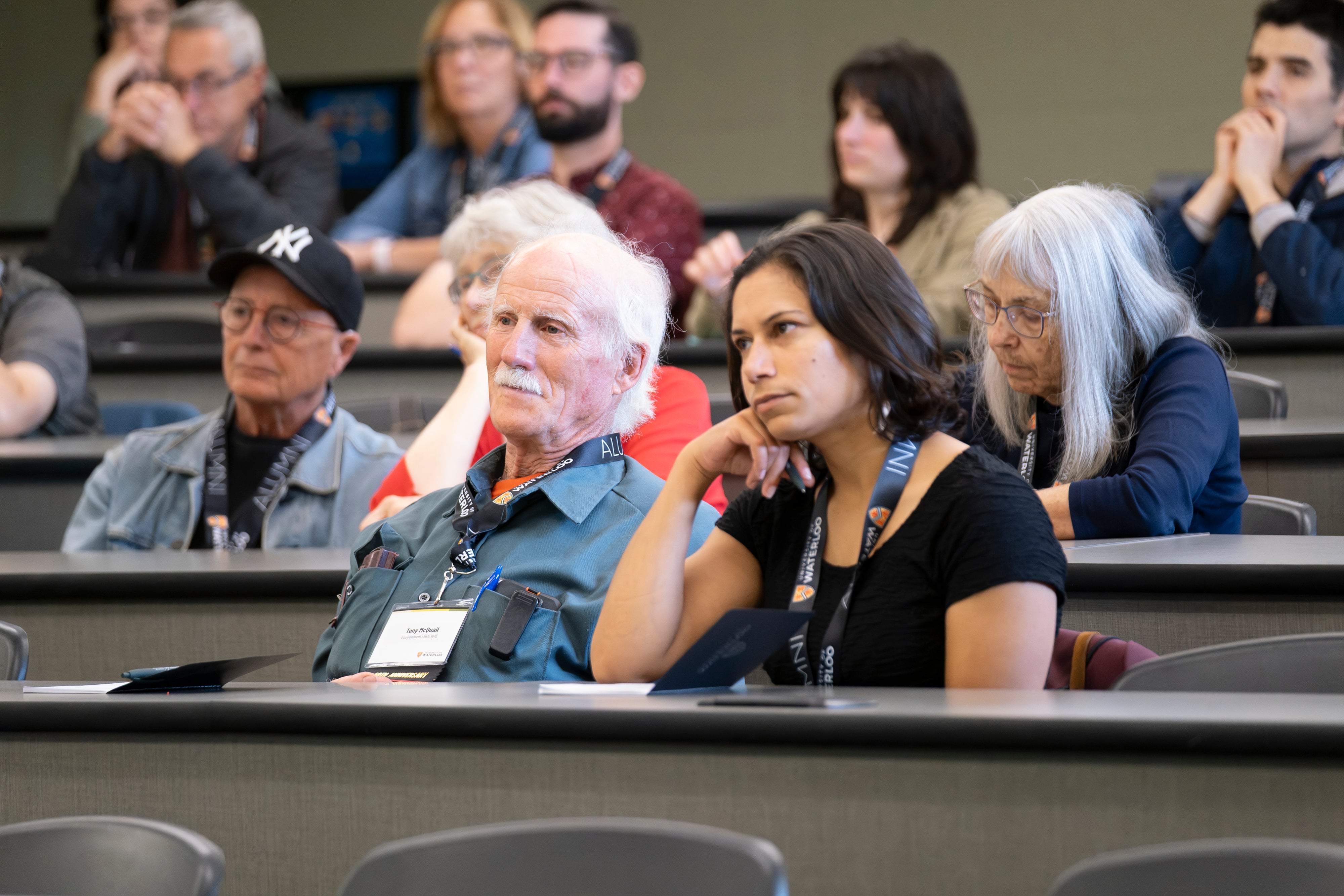 A diverse group of people sit in a lecture hall, listening. 