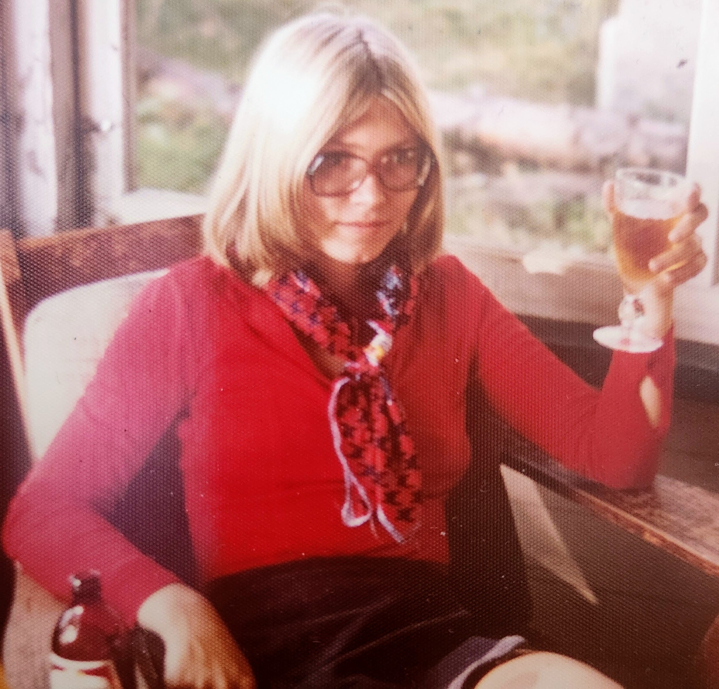 Young blond woman in red sweather with scarf hold a wine glass.
