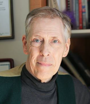 white  man with grey-salt and paper hair smiling at camera in a grey turtle neck