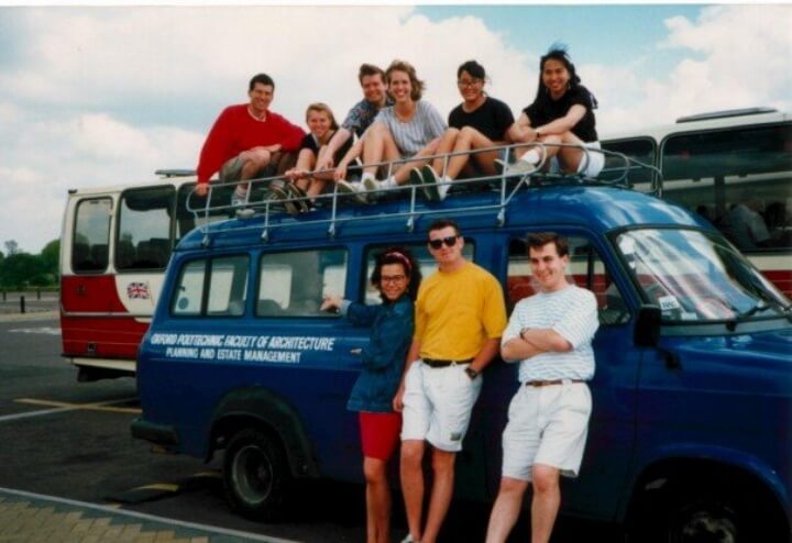Students posed in front of and sitting on top of a blue van