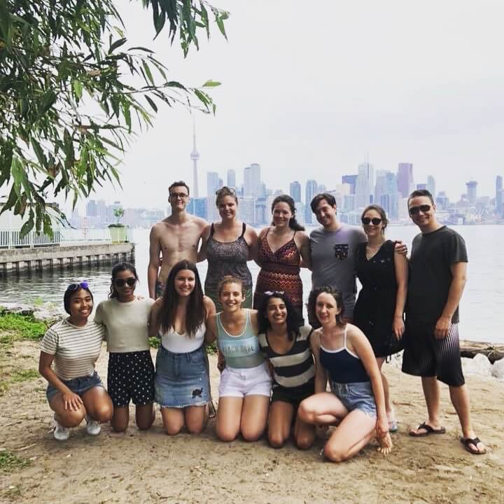 Group of university students smiling at a beach with the Toronto skyline behind them