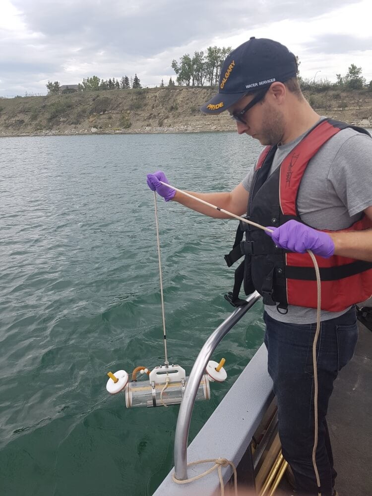 Student on edge of boat holding tube device over the water by a cord