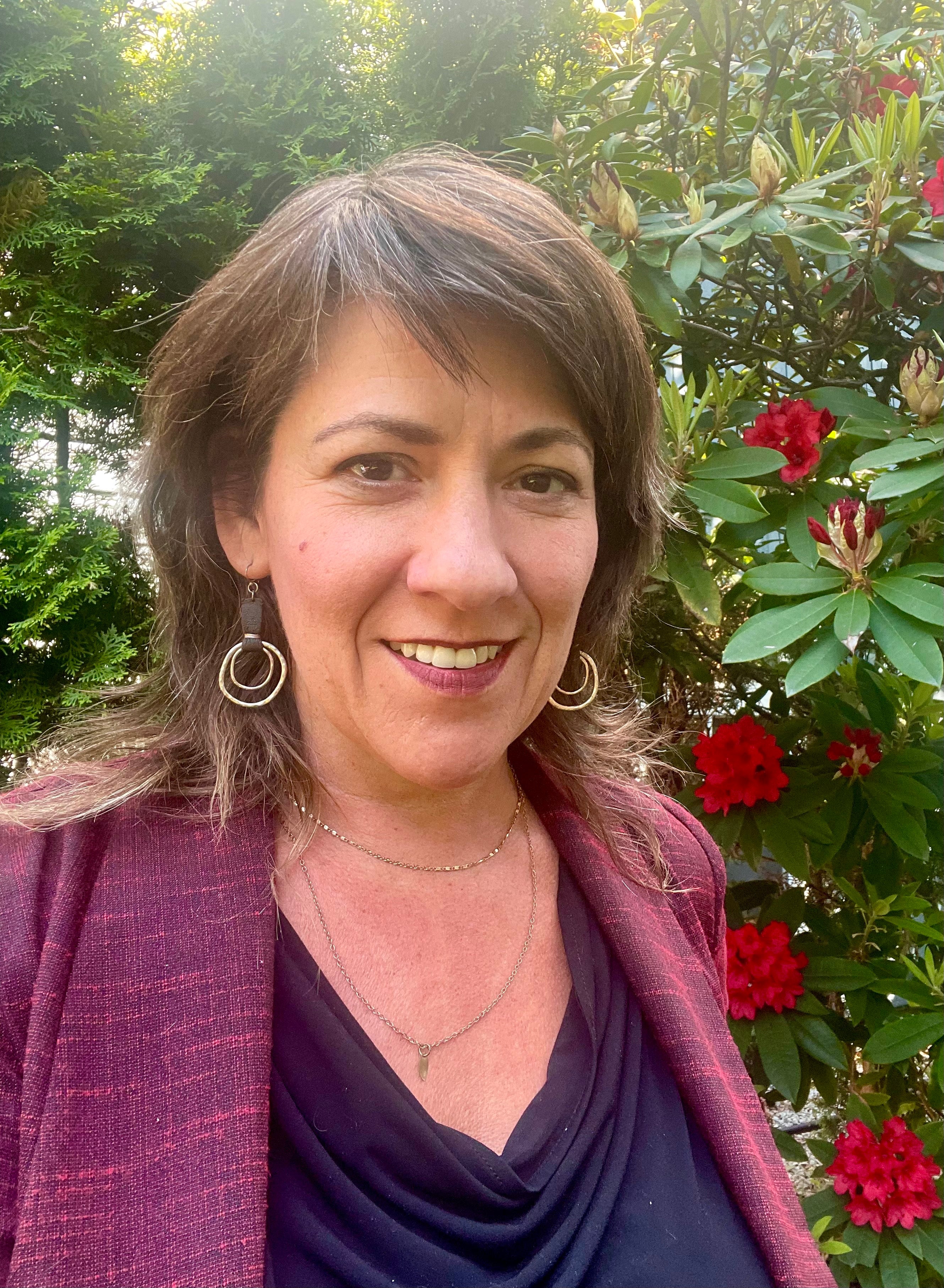 woman smiling at the camera in a pink blazer, dark purple top and 2 layered chain necklaces