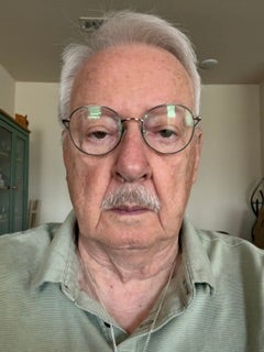 Older man with glasses and grey hair looks ahead.