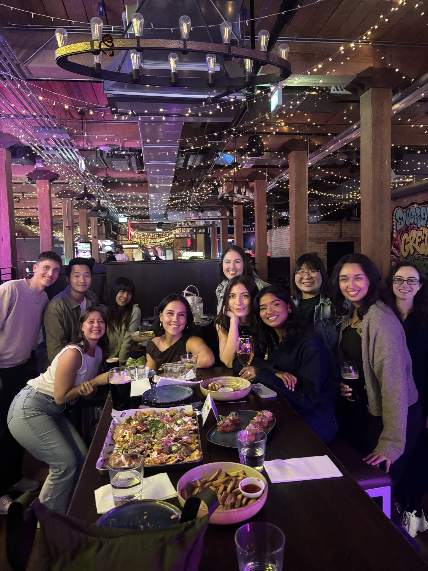 A diverse group of people posing together at a table in a lively restaurant with dim lighting and decorations.