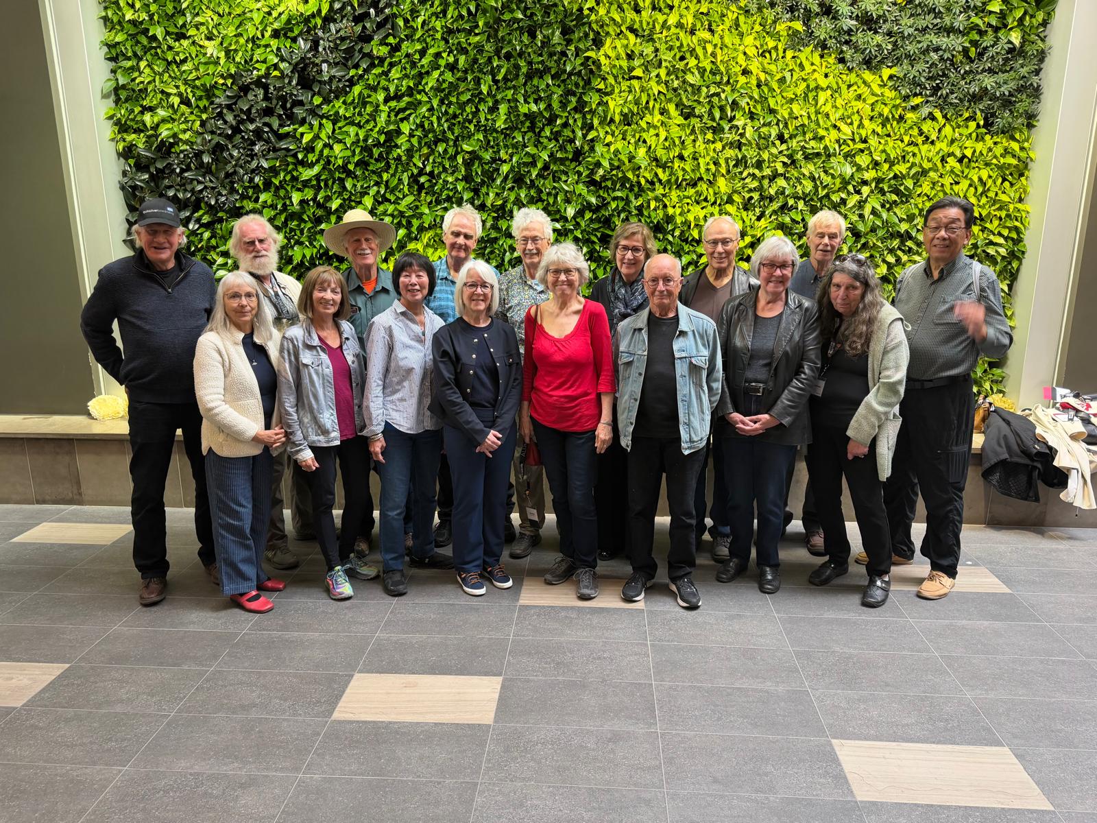 A group of people standing together in front of a green wall made of plants.