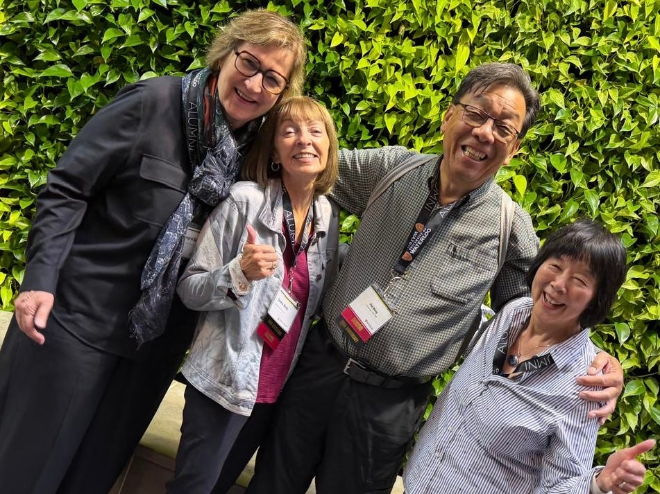 Four people posing together in front of a green wall.