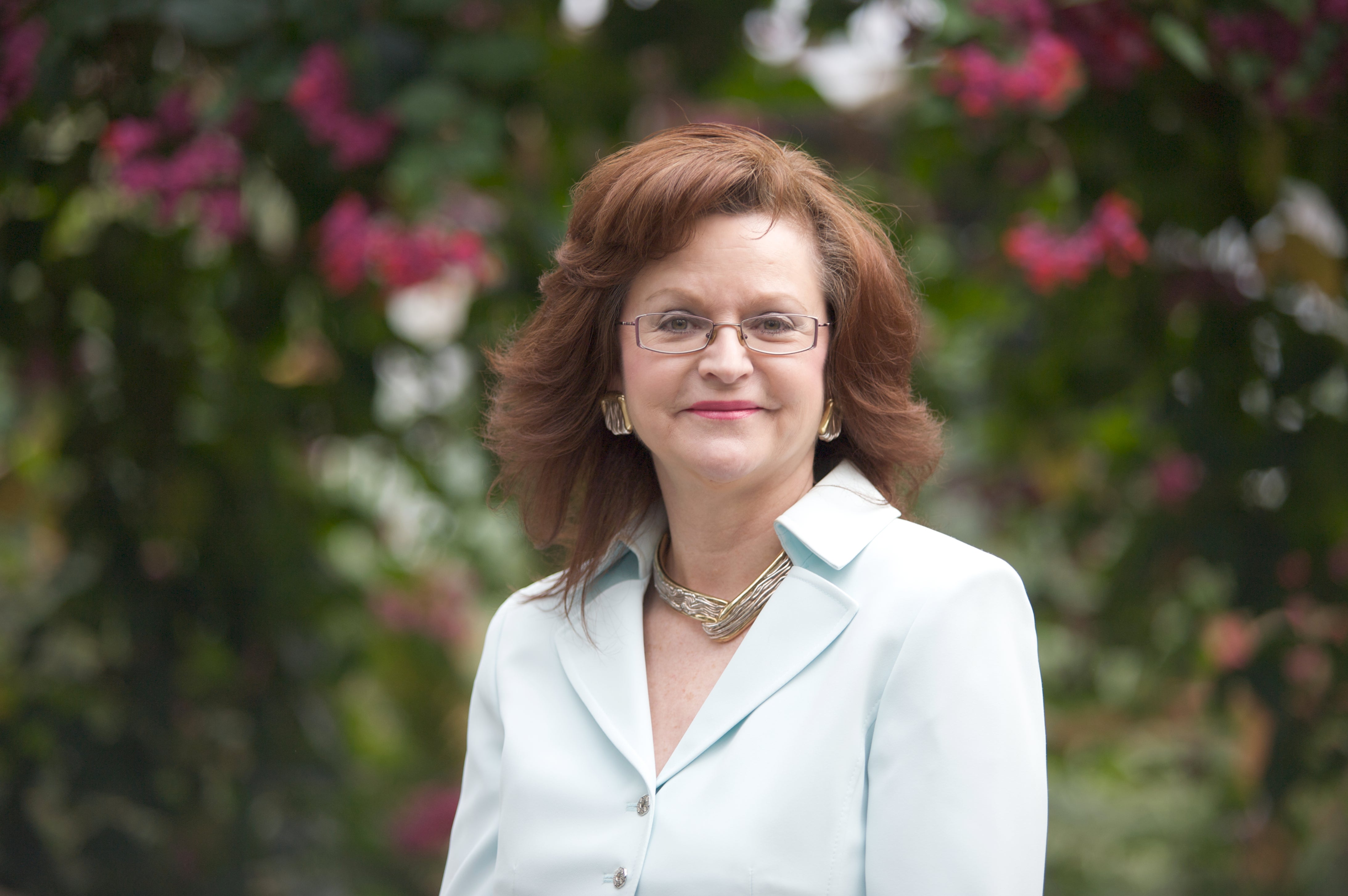 Woman with brown hair and white jacket and glasses. 
