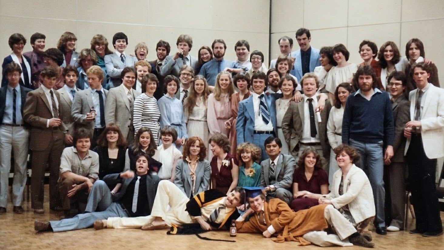 A large group of people gathered for a photo, dressed in a mix of formal and casual attire, with some wearing suits and others in dresses.