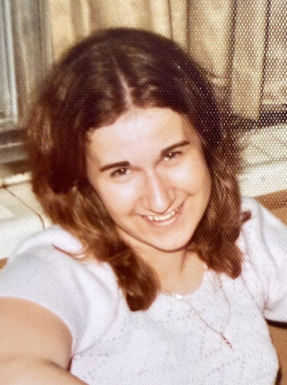 Woman with brown hair and white top smiles with head to one side.