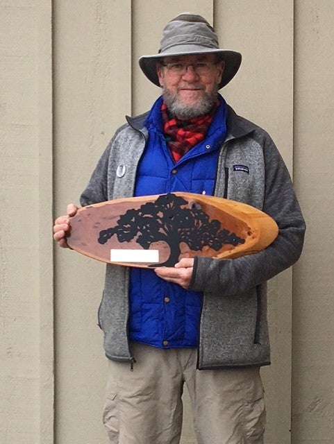 Man with grey hat and glasses holds plaque.