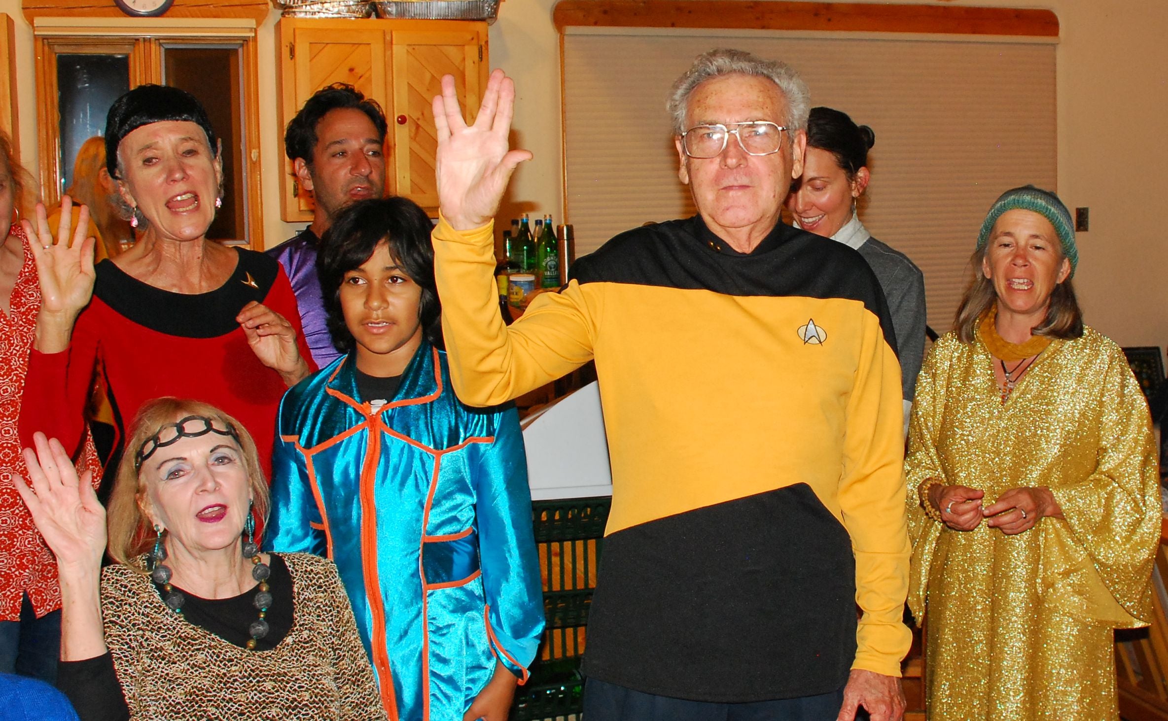 People in star trek uniforms hold hands up with middle and ring fingers spread.