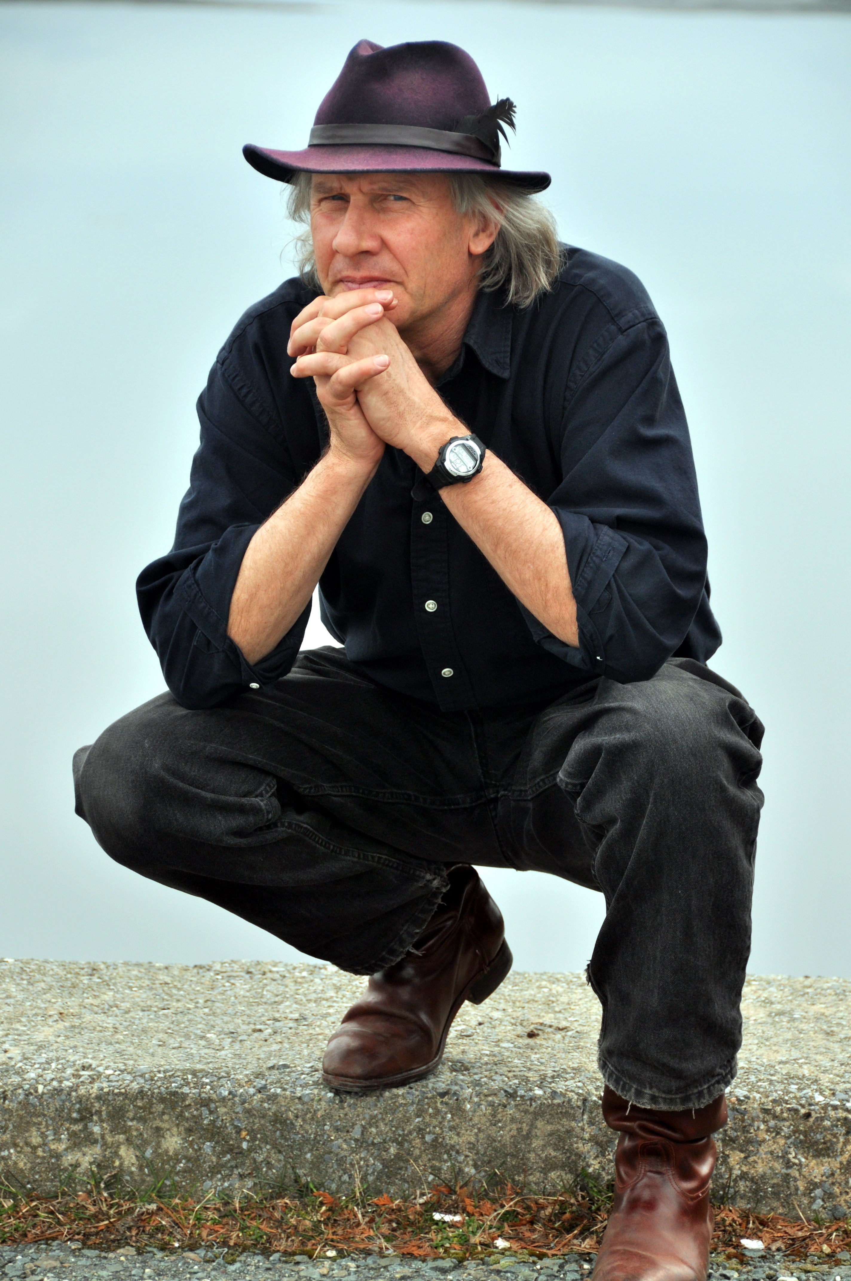 Man dressed in black with black cowboy hat crouches.