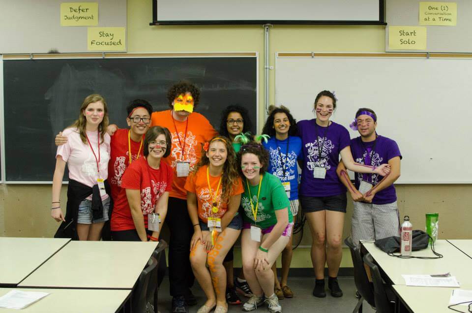 Group of university students wearing orientation gear standing at the front of a classroom and smiling