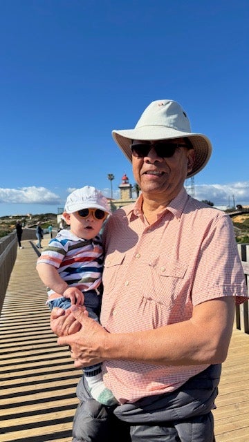 Man with white hat holds a babby in a striped shirt. 