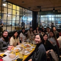 A group of people sit around a restaurant table with food and drinks, smiling at the camera.