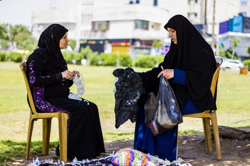 Two Afghan women work on crafts in the shade