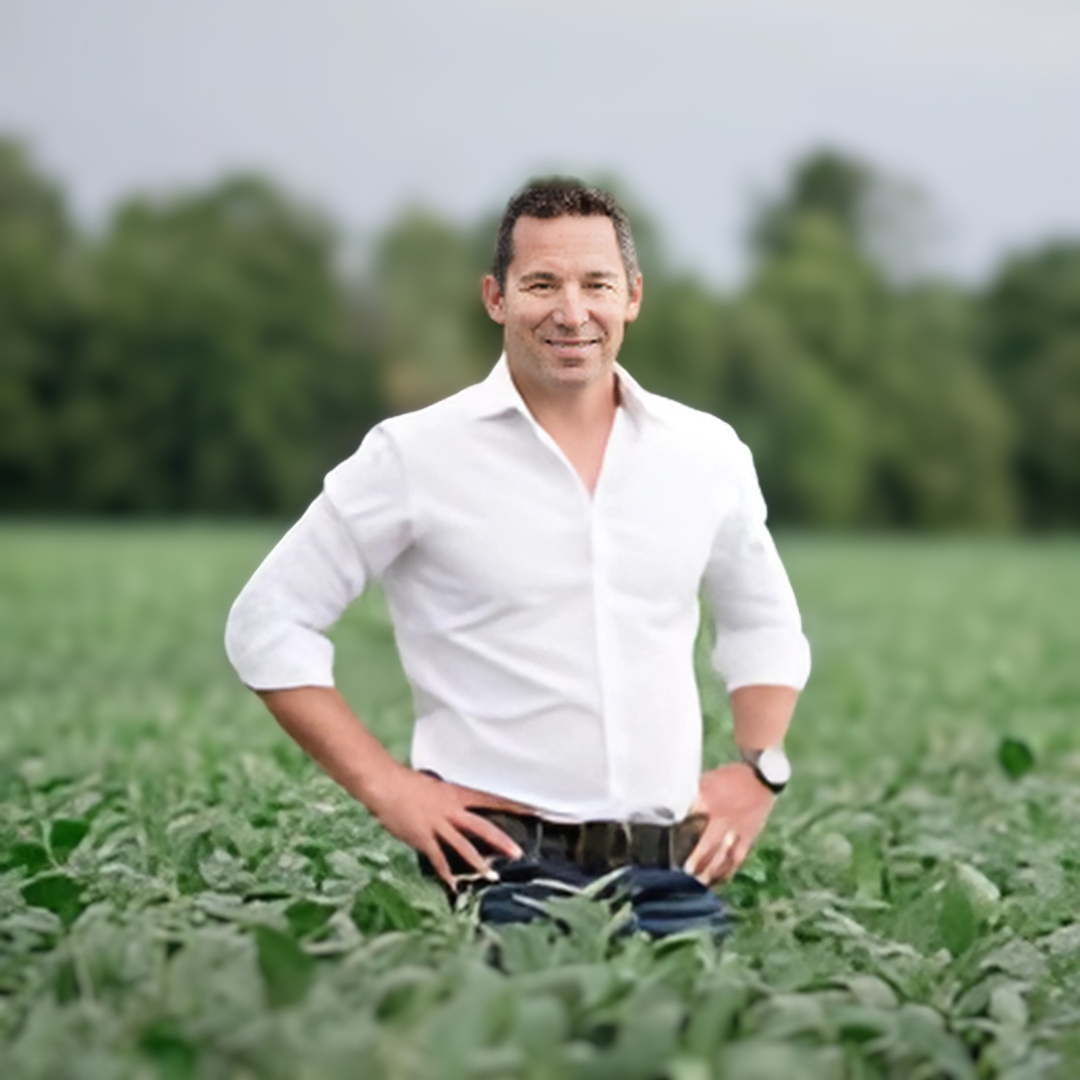 a man standing in a field wearing a white shirt with a smile on their face