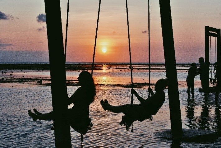 two people on swings by the water during sunset