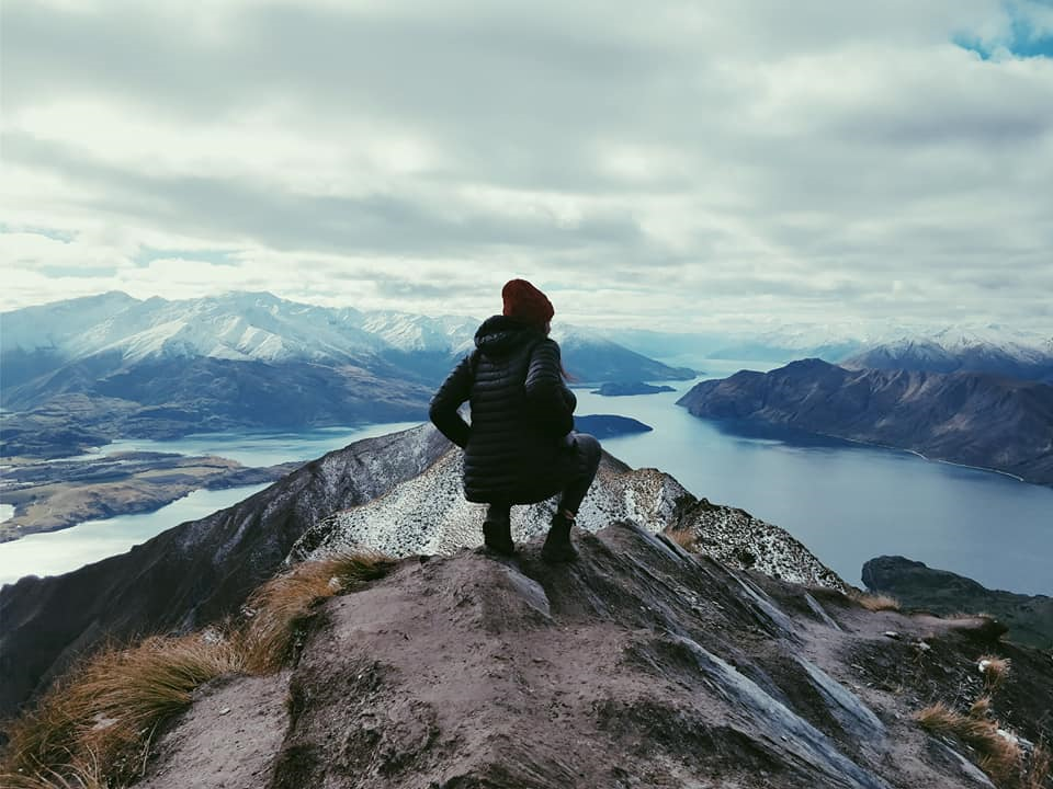 Female student standing on Roys Peak in New Zealand with her back to the camera, looking at the water.