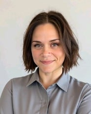 Portrait of a smiling woman with short brown hair wearing a gray button-up shirt against a light background.