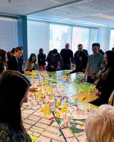 Group gathered around a city model, discussing urban planning and placing yellow building markers.