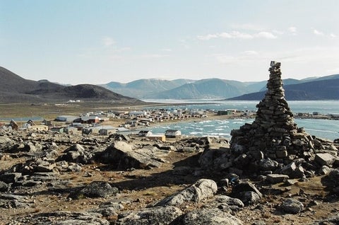 A rock sculpture with a small coastal town in the background.