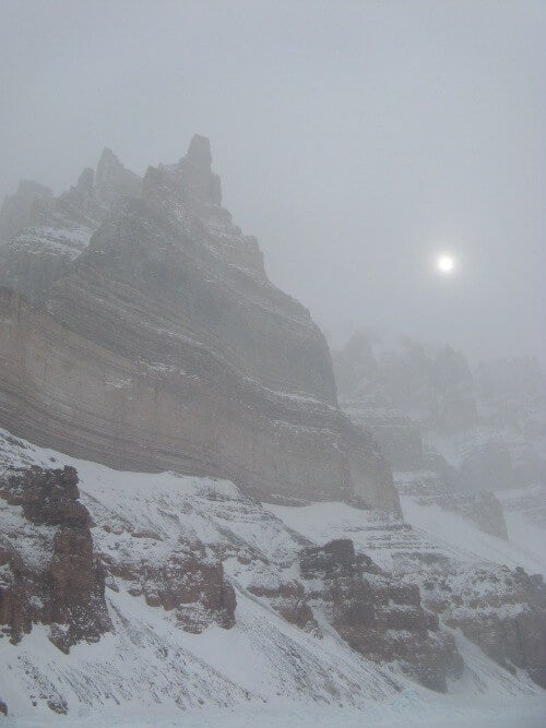 Sun behind a cliff on a snowstorm.