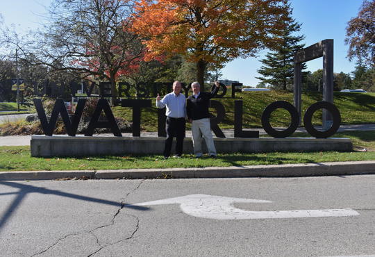 Larry Hundt and Chris Flemming stand in front of the University of Waterloo entrance sign