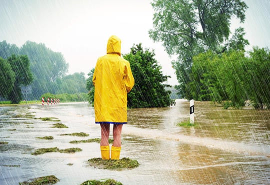 A person wearing a yellow raincoat standing on flooded road