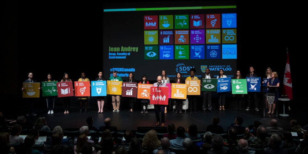 People on the stage holding up the SDGs during the SDSN Canada launch event.